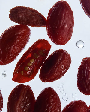 Close-up of several dark red goji berries on a white background, with one goji sliced open to show the inner seed cavity and small air bubbles.