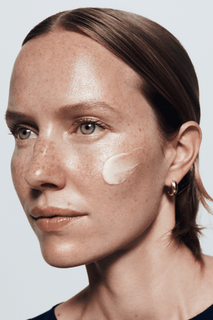 Close-up of a woman's face with skincare product application on a light gray background